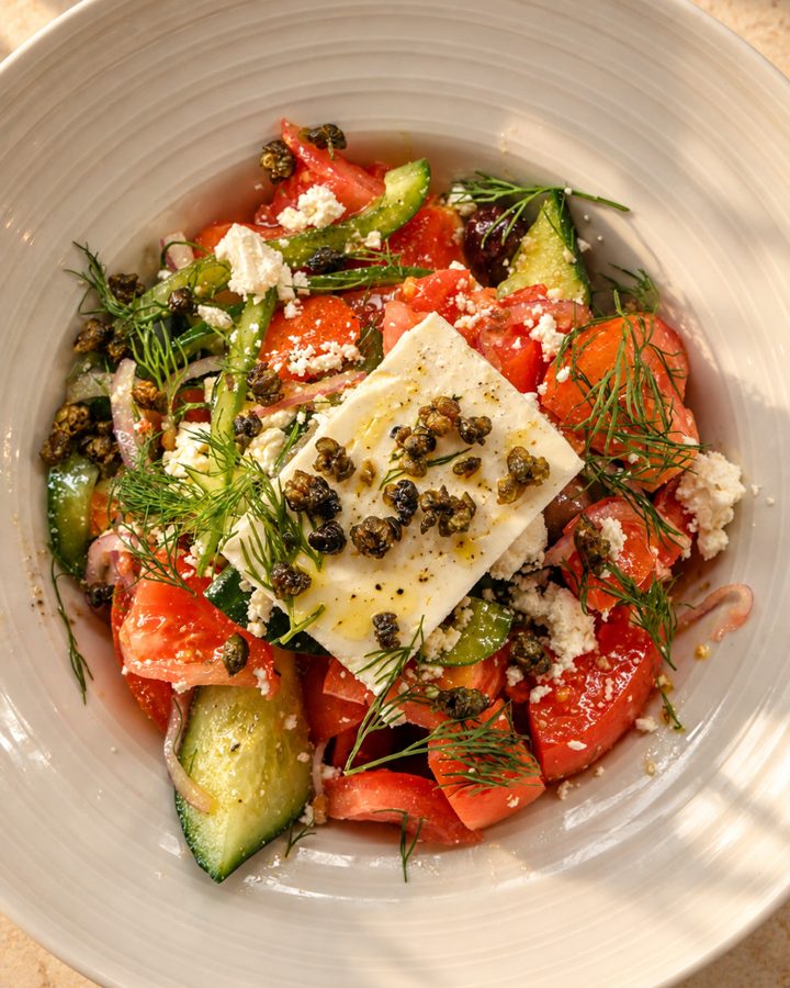 Greek salad with a block of feta, tomato, cucumber and dill